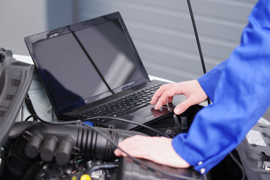 mécanicien utilisant un ordinateur connecté au moteur pour réparer le véhicule