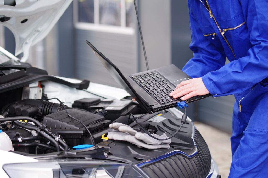 mécanicien effectuant des réglages électroniques avec un ordinateur connecté au moteur du véhicule